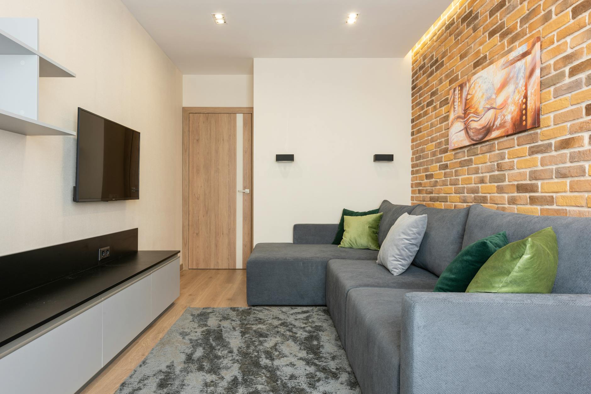 Przytulny nowoczesny salon z ceglaną ścianą, szarą sofą i oświetleniem LED