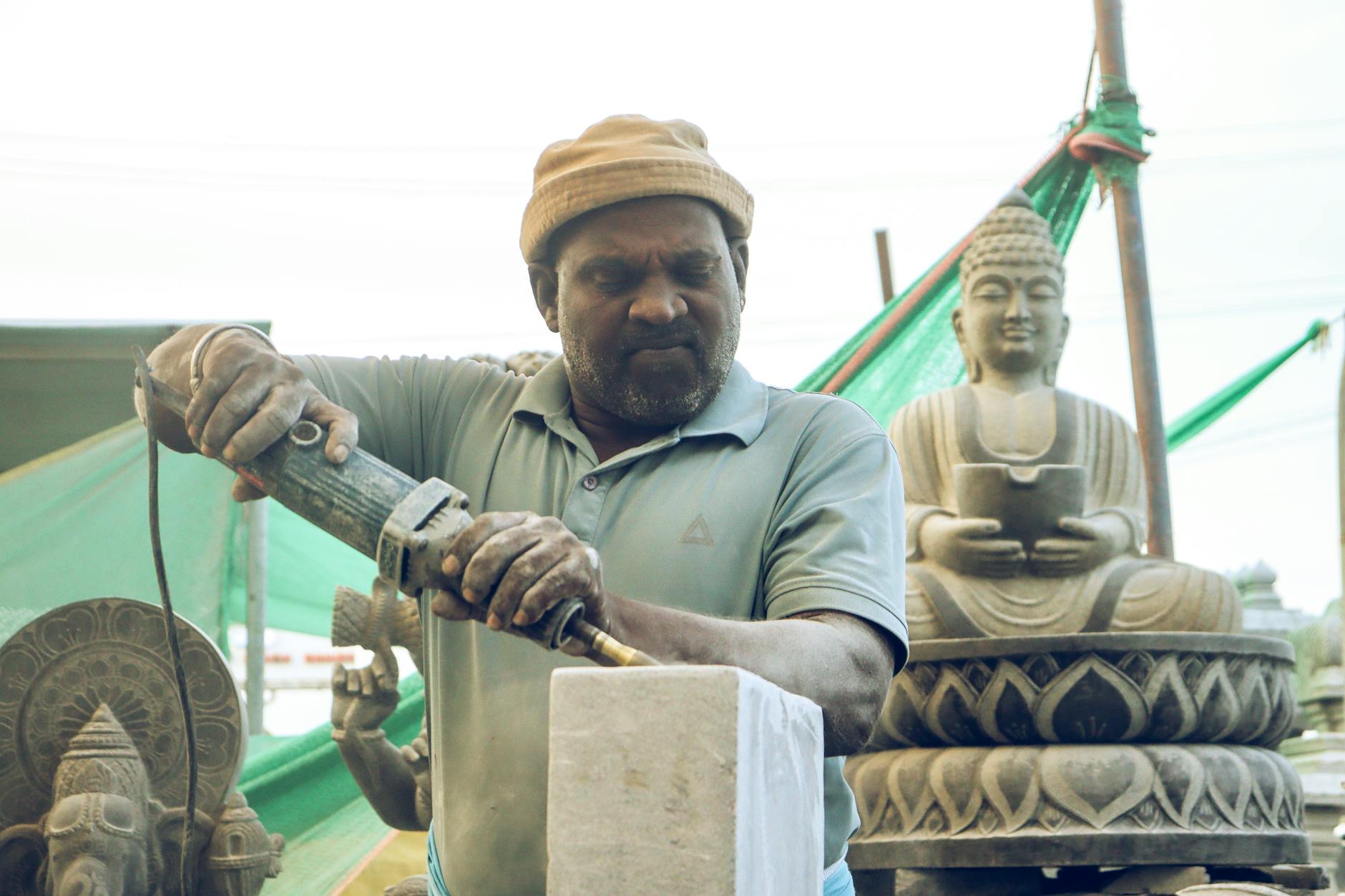 Rzeźbiarz w pracowni dłutuje kamienną rzeźbę wśród gotowych figur