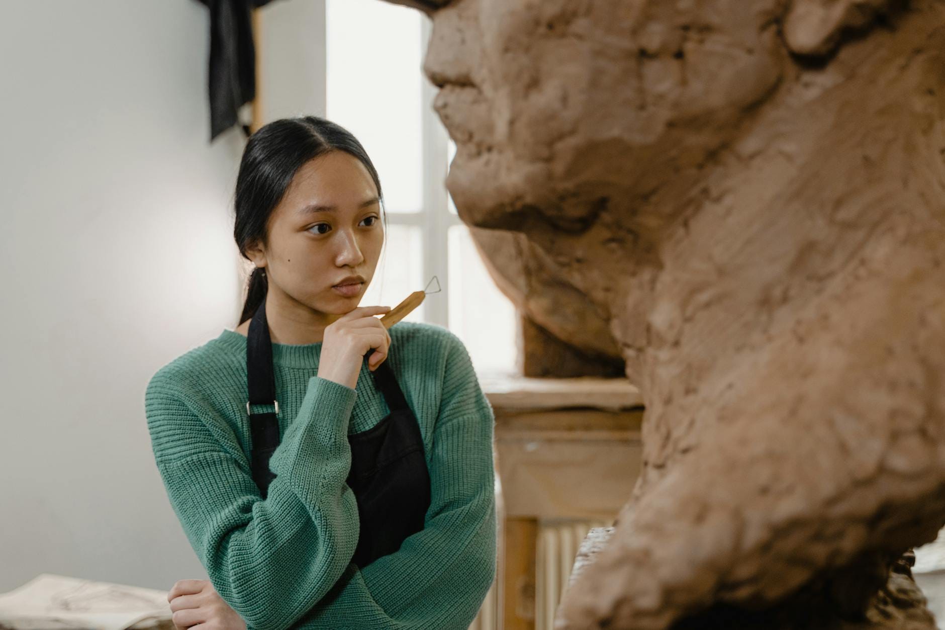 Rzeźbiarz w zielonym swetrze pracuje nad dużą glinianą rzeźbą w pracowni