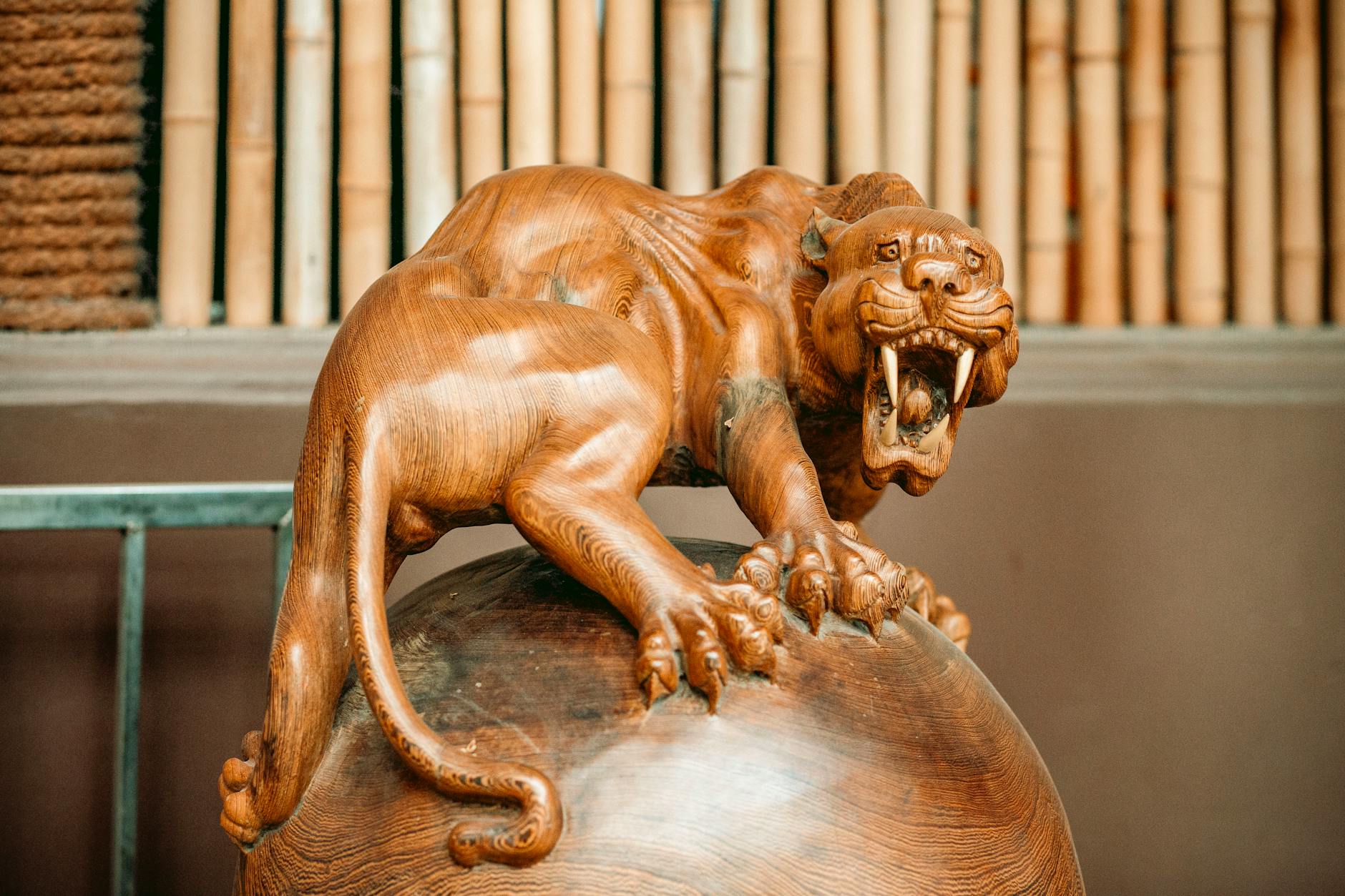 Drewniana rzeźba tygrysa na kuli na tle bambusa