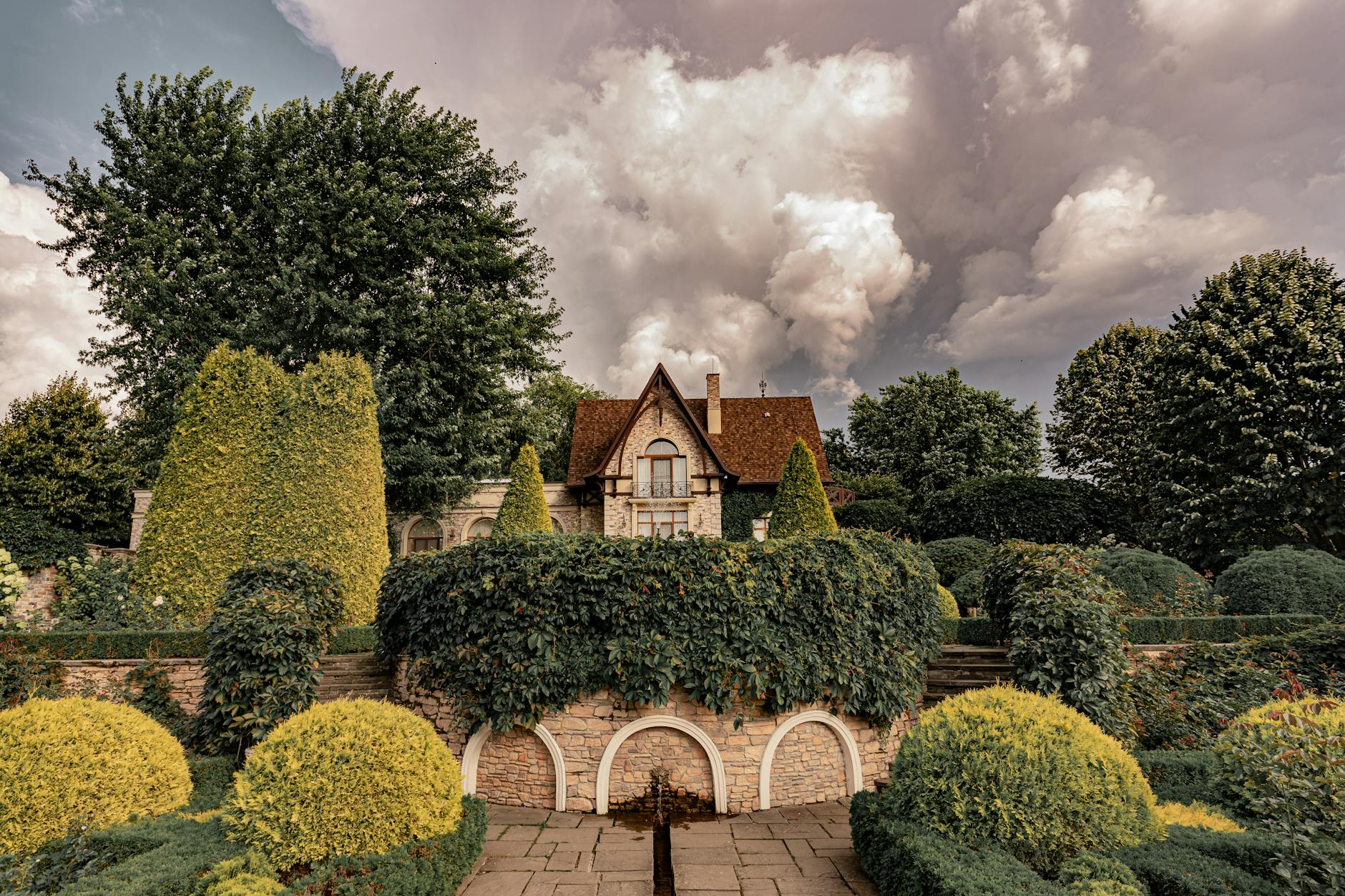 Elegancki dwór wśród równo przyciętych krzewów na tle burzowego nieba