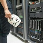 Osoba trzyma maskę anonimowego przy serwerach, motyw cyberbezpieczeństwa