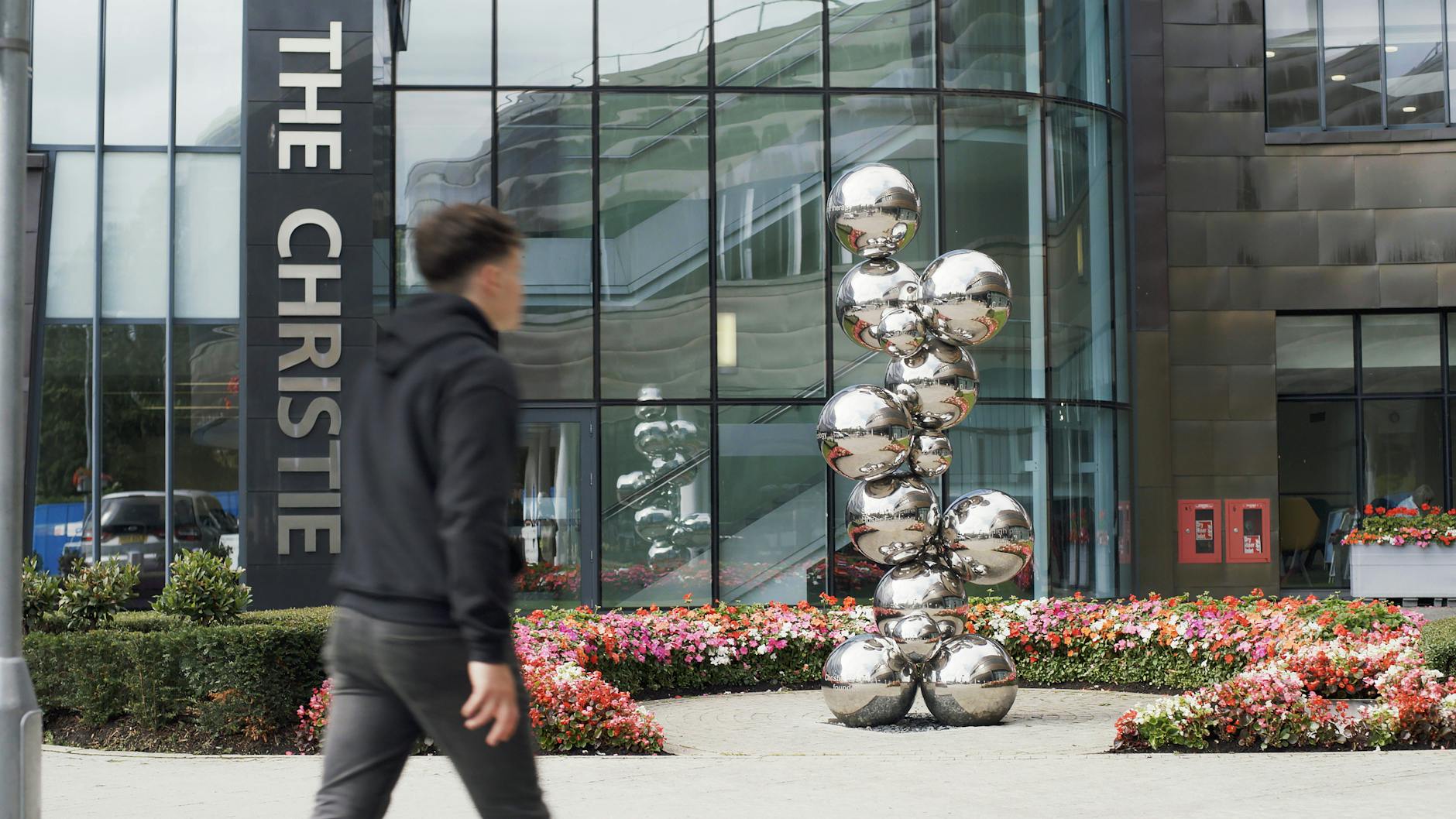 Przechodzień mija nowoczesną lustrzaną rzeźbę przy wejściu do budynku