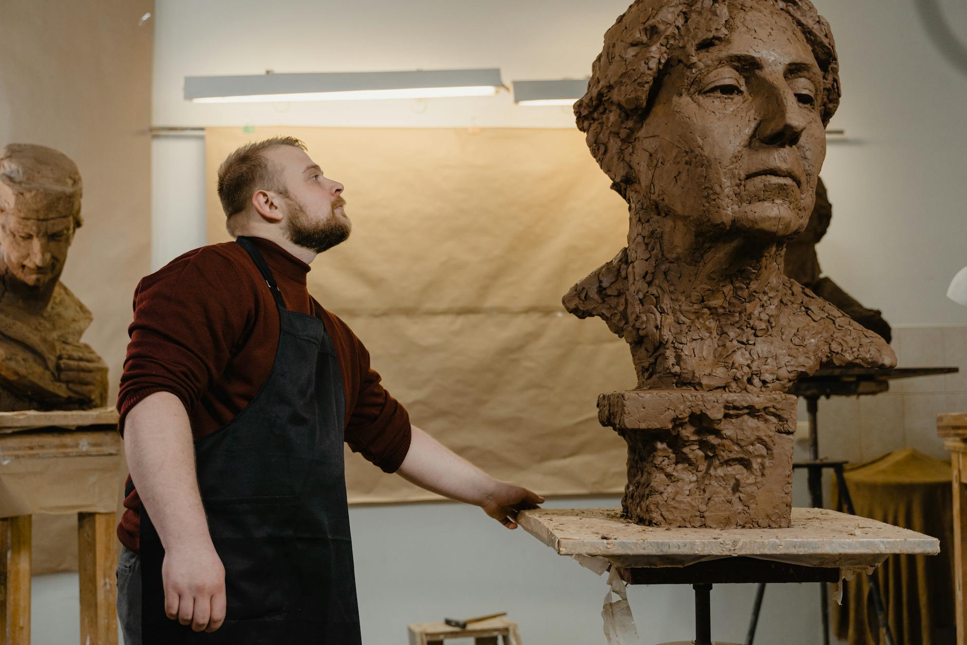 Rzeźbiarz w fartuchu modeluje szczegółowe popiersie z gliny w pracowni