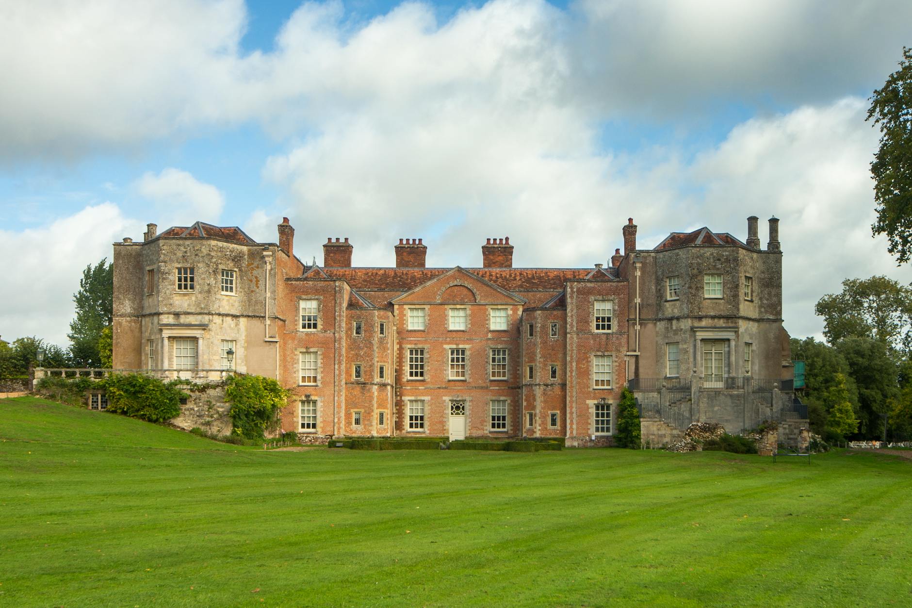 Zabytkowy dwór angielski otoczony zielenią w słoneczny dzień