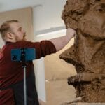Artysta rzeźbi gliniany bust w jasnej pracowni rzeźbiarskiej