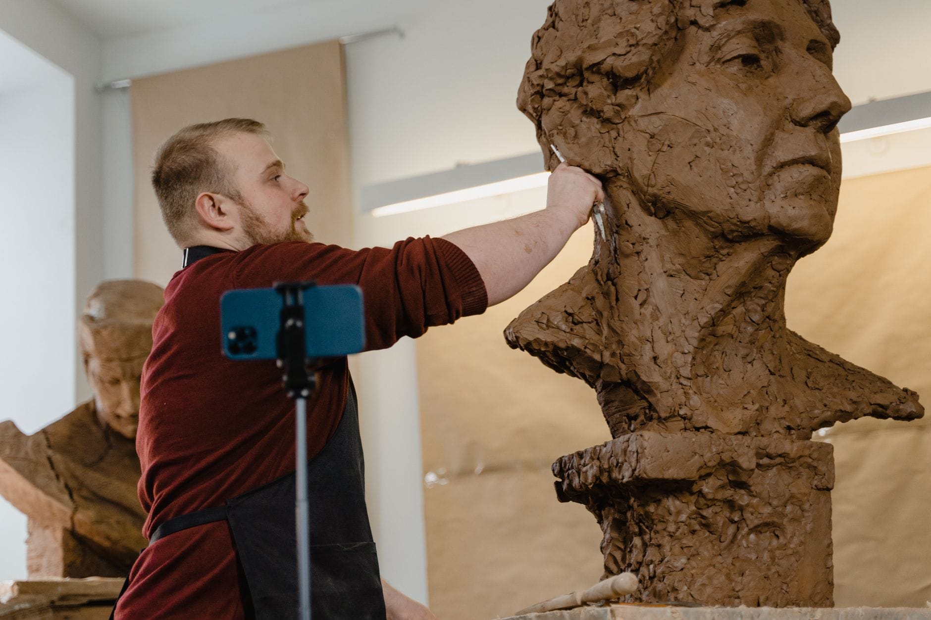 Artysta rzeźbi gliniany bust w jasnej pracowni rzeźbiarskiej