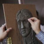 Zbliżenie dłoni rzeźbiących gliniany portret w pracowni