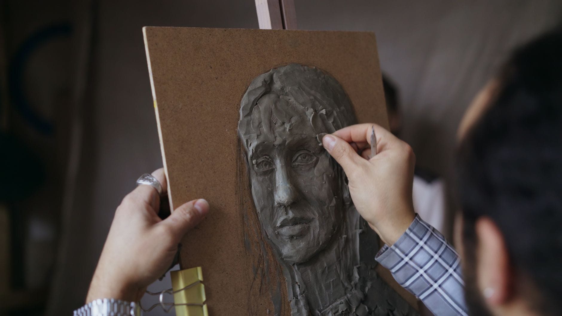 Zbliżenie dłoni rzeźbiących gliniany portret w pracowni