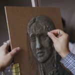 Dłonie rzeźbiące portretowy relief z gliny w pracowni